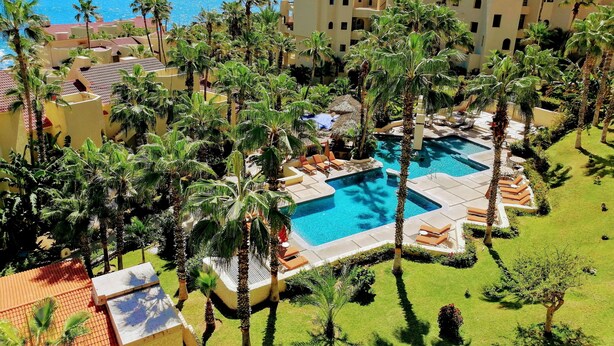 Un complexe hôtelier doté d’une piscine entourée de palmiers et offrant une vue sur l’océan.