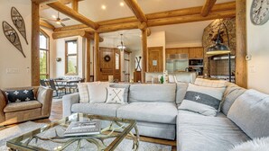 A spacious living area with a large sofa, a glass coffee table, and a dining area with chairs. - Hilltop Breck Home: Hot Tub, Views & Walk to Town (Breckenridge)