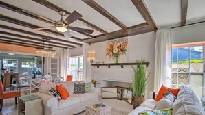 A spacious living room with a white sofa, a coffee table, and a fireplace. There is a ceiling fan, a chandelier, and a large window with curtains. - Waterfront Port Isabel Family Home w/ Pool & Pier! (Port Isabel)