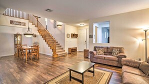 A spacious living room with hardwood flooring, a dining area with wooden furniture, a brown leather sofa, and a staircase leading to another level.