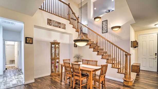 A spacious dining area with a wooden table and chairs, a staircase with wooden railings, and a hanging light fixture.