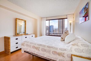 A bedroom with a large bed, a dresser, a mirror, and a city view through the window.