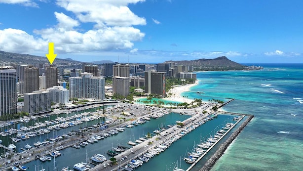 Un port de plaisance où sont amarrés de nombreux bateaux, une plage et, au loin, des immeubles de grande hauteur.