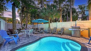 A backyard with a swimming pool, patio furniture, and a barbecue grill.
