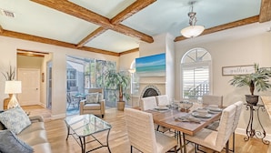 A spacious living room with a wooden ceiling, a dining area with a large table and chairs, and a view of the outdoors through large windows.