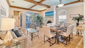 A spacious living room with a high ceiling, wooden beams, a dining area with a table and chairs, and a view of the outdoors.