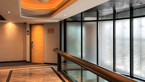 Un vestíbulo de hotel moderno con una puerta de madera, una barandilla de vidrio y un ventanal con paneles de vidrio esmerilado.