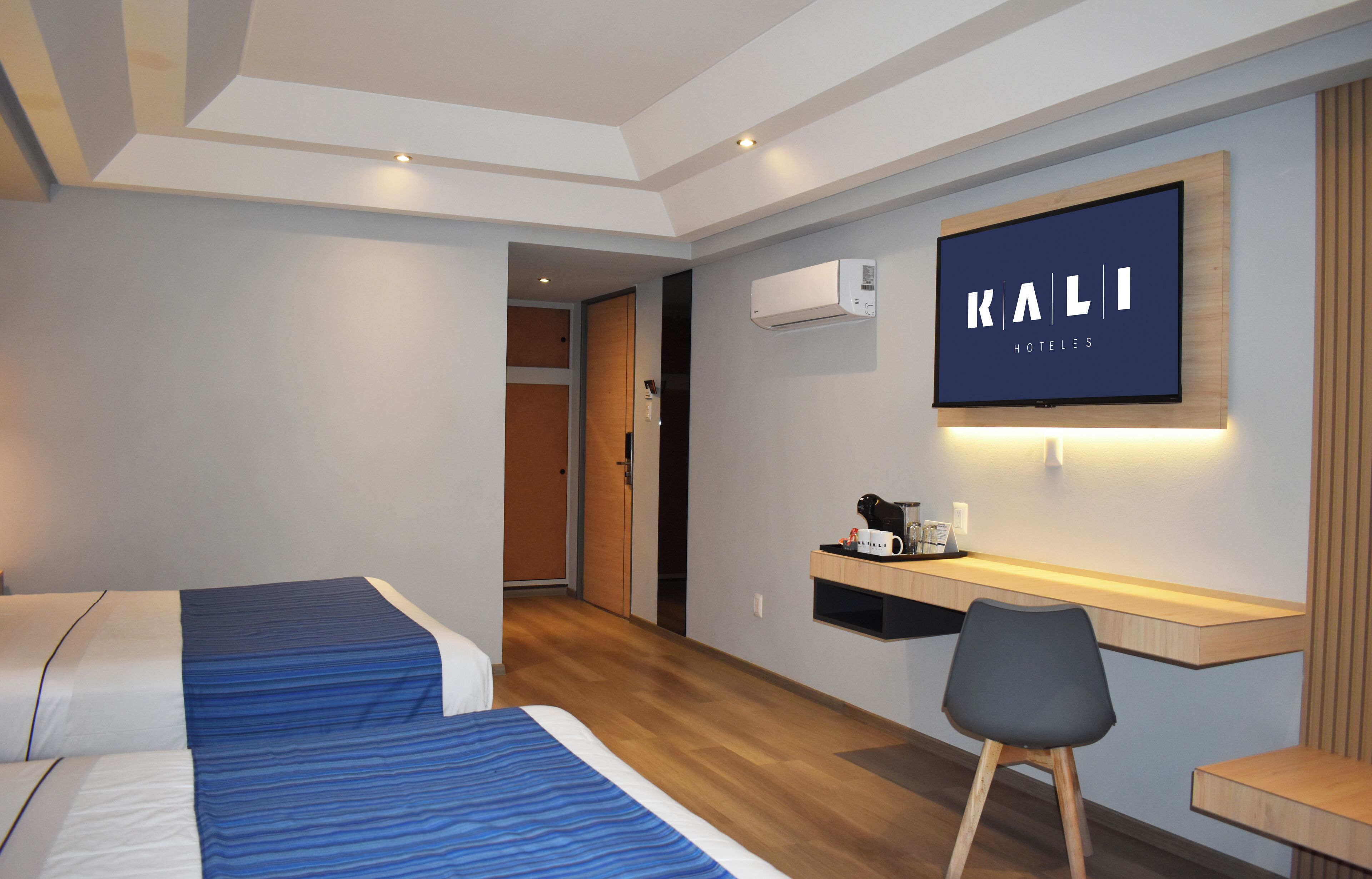 A hotel room with a bed, a desk, a chair, a flat-screen TV, and an air conditioning unit.