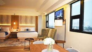 Habitación de hotel con una cama grande, un escritorio, una silla y vistas a un paisaje urbano a través de la ventana.