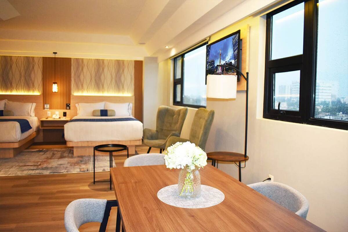 A hotel room with a large bed, a desk, a chair, and a view of a cityscape through a window.