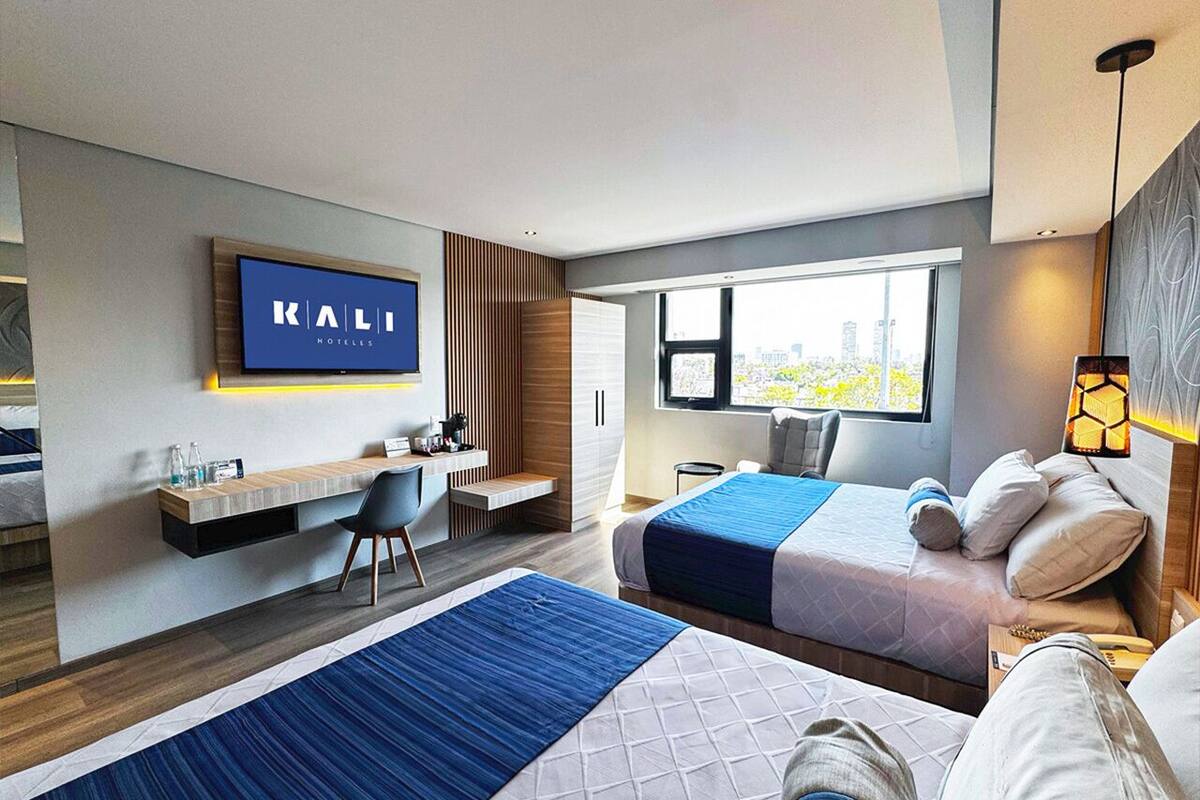 A hotel room with two beds, a desk, a TV, and a city view.