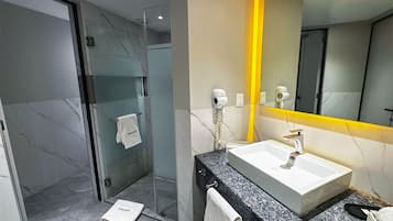 A modern bathroom with a glass shower enclosure, a white sink with a marble countertop, and a mirror with a yellow frame.