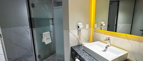 Une salle de bain moderne avec une douche à l’italienne en verre, un lavabo blanc doté d’un plan de travail en marbre et un miroir avec un cadre jaune.