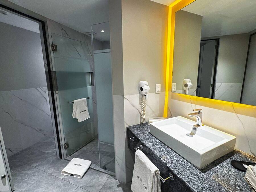 A modern bathroom with a glass shower enclosure, a white sink with a marble countertop, and a mirror with a yellow frame.