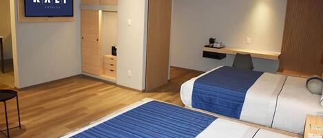 A hotel room with two beds, a TV, a wardrobe, and a desk with a chair.