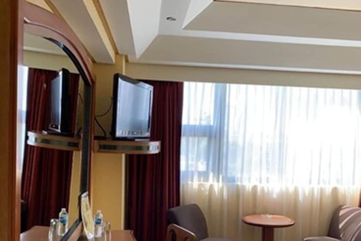 Habitación de hotel con cama, escritorio y silla, televisor, una mesita y ventana con cortinas.