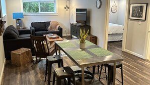 Una sala de estar moderna con comedor, un sofá, un televisor y una ventana con vistas a zonas verdes.