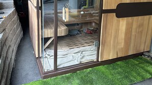 Una sauna con paredes de vidrio, bancos de madera y un perchero visible para toallas.