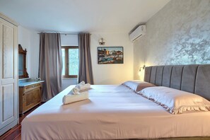 Une chambre d’hôtel avec un grand lit, une commode en bois, un tableau au mur et un appareil de climatisation.