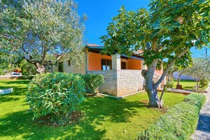 Une maison à la façade en pierre, entourée d’une pelouse et d’arbres bien entretenus.