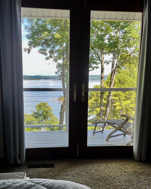 A room with a large sliding glass door leading to a balcony with a view of a lake and trees.
