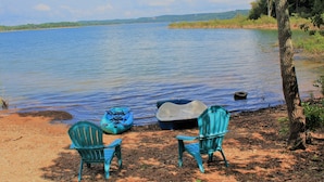 A lakeside scene with two chairs and a kayak by the water. - Luxury Waterfront Resort Home with Private Beach! (Rogers)