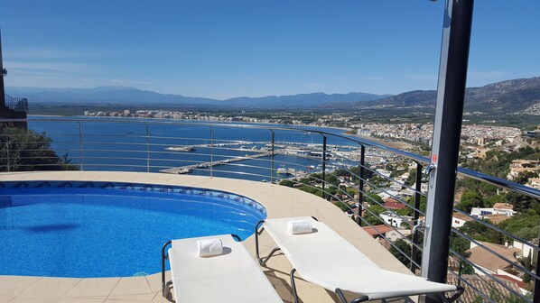 A pool area with two sun loungers and a view of a marina and cityscape.