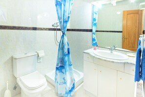 A bathroom with a toilet, shower, sink, and mirror.