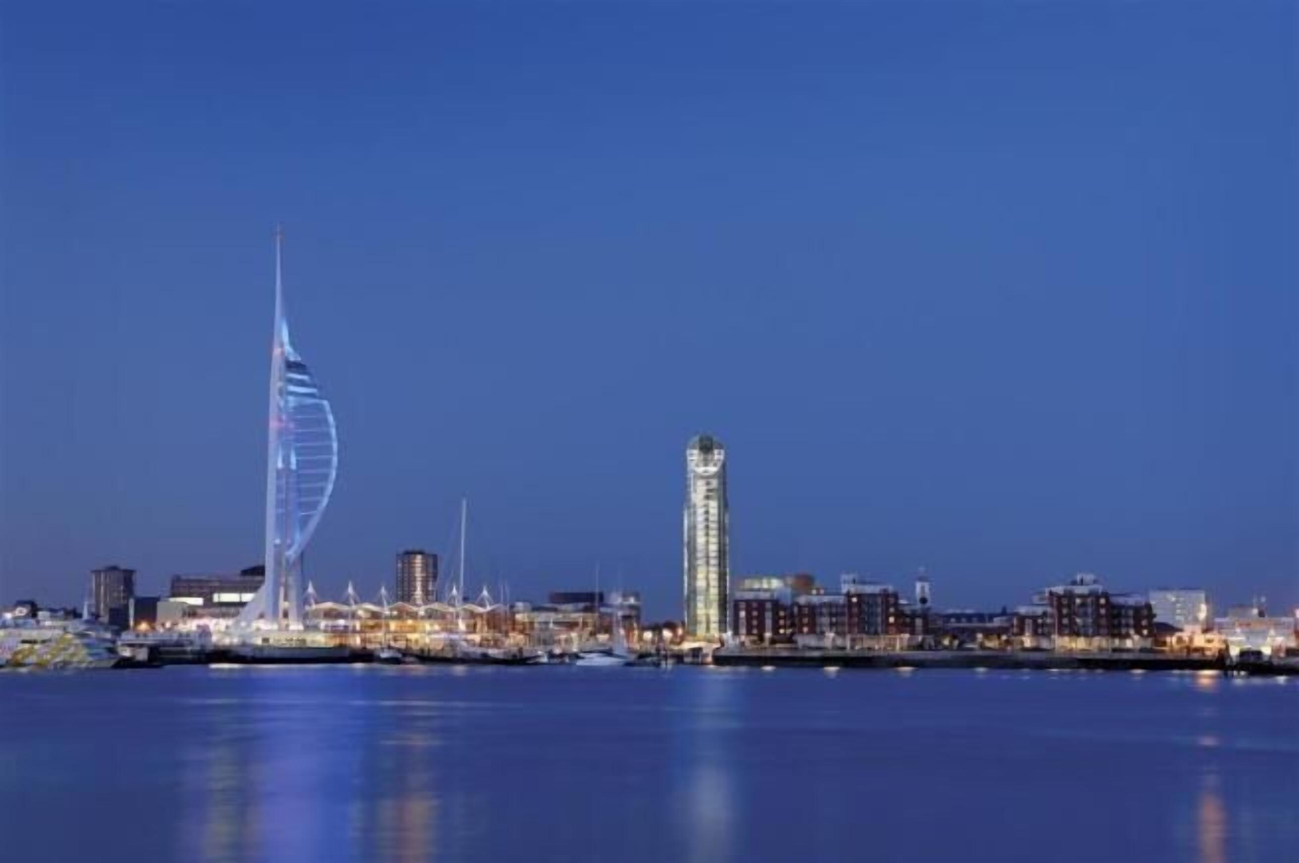 A waterfront cityscape with a prominent sail-shaped building and a tall tower.