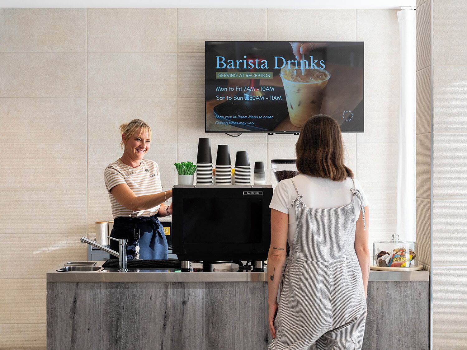 Un barista sert un client dans un espace d’accueil équipé d’un écran affichant un menu numérique.