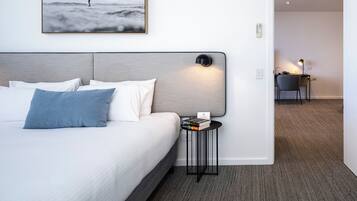 Habitación de hotel con cama, mesita de noche con lámpara, un cuadro en la pared y un escritorio con silla al fondo.