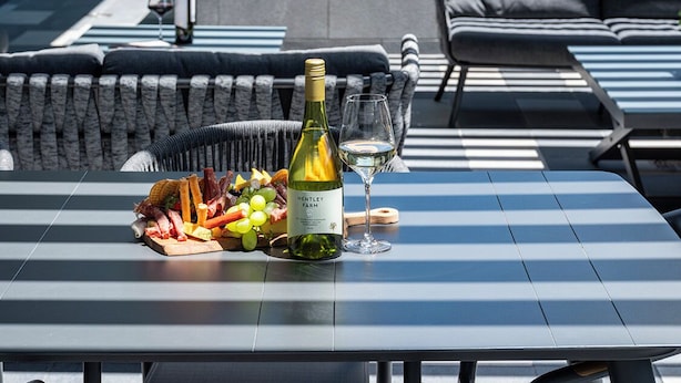 An outdoor seating area with a table, a bottle of wine, and a glass. - Quest Robina (Robina)