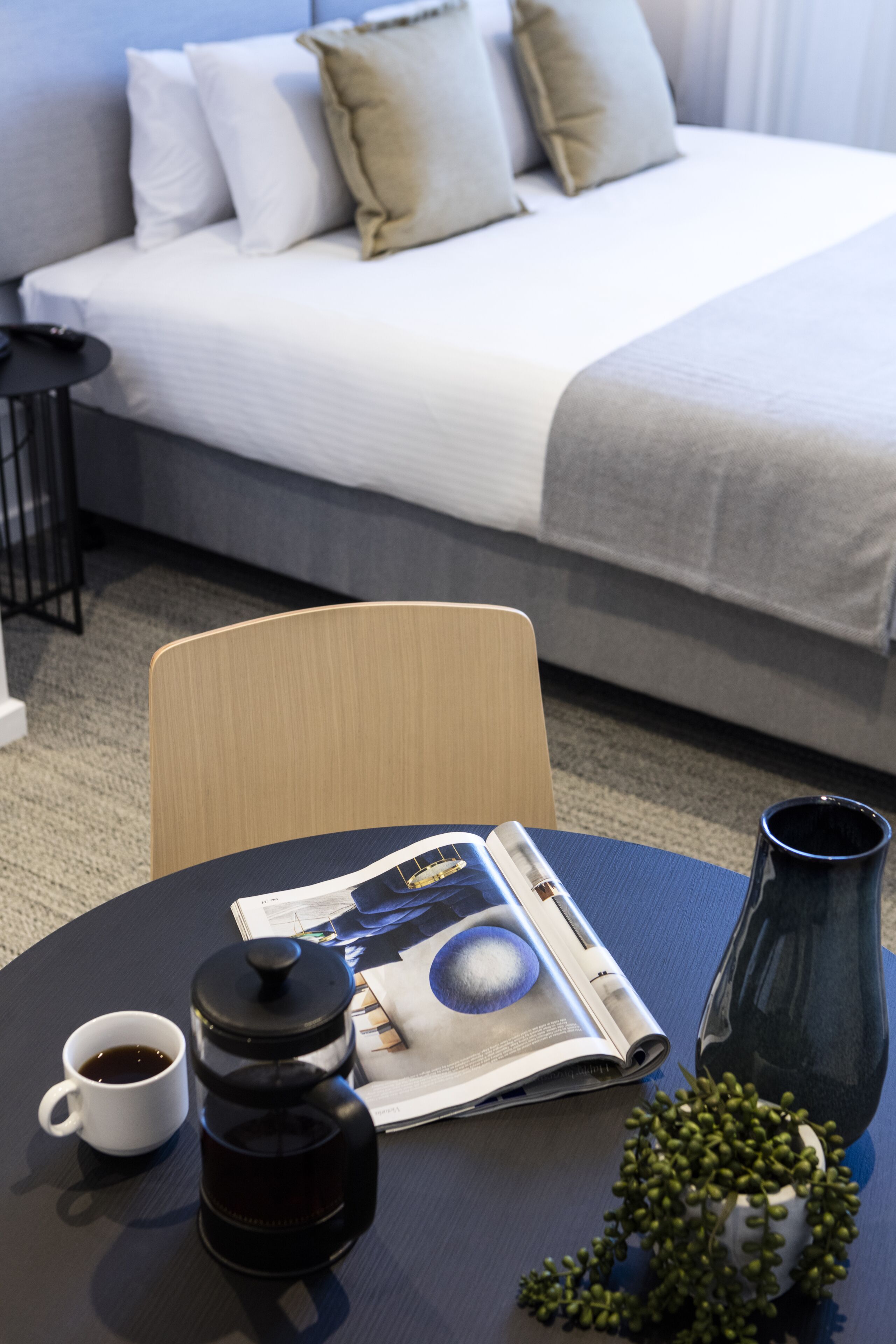 A neatly arranged hotel room with a bed, a coffee table, a cup of coffee, a newspaper, and a vase.