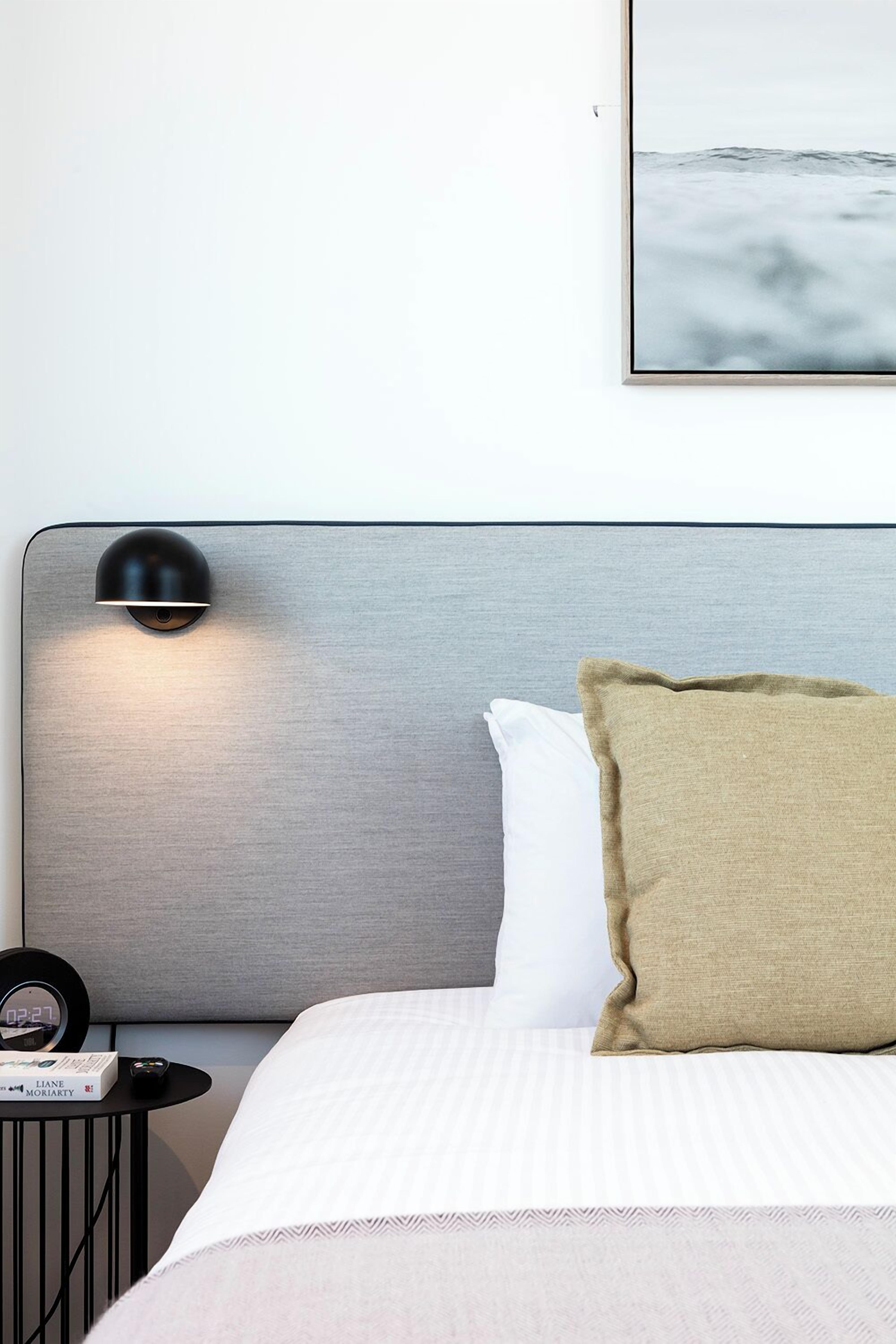 A neatly made bed with a headboard, a bedside table with a lamp, and a framed picture on the wall.