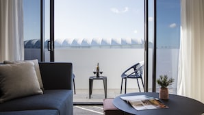 A modern room with a sofa, a small table with a plant, and a view of a building with a unique roof design. - Quest Robina (Robina)