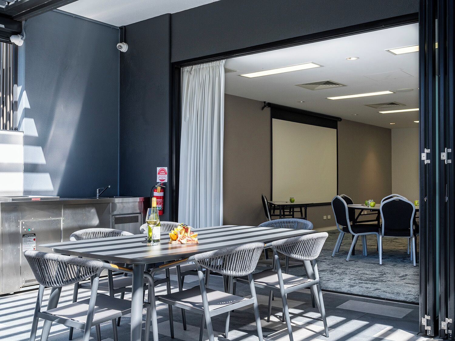 A modern conference room with a large table, chairs, a projector screen, and a fire extinguisher.