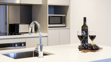 A modern kitchen with stainless steel appliances, a built-in microwave, and a wine bottle with glasses on the counter.
