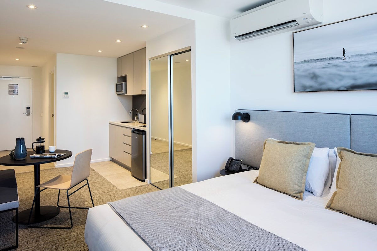 Una habitación de hotel moderna con cama, mesita de noche y una pequeña cocina.