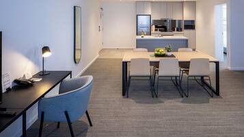 A modern hotel room with a dining area, a kitchen, and a large mirror.