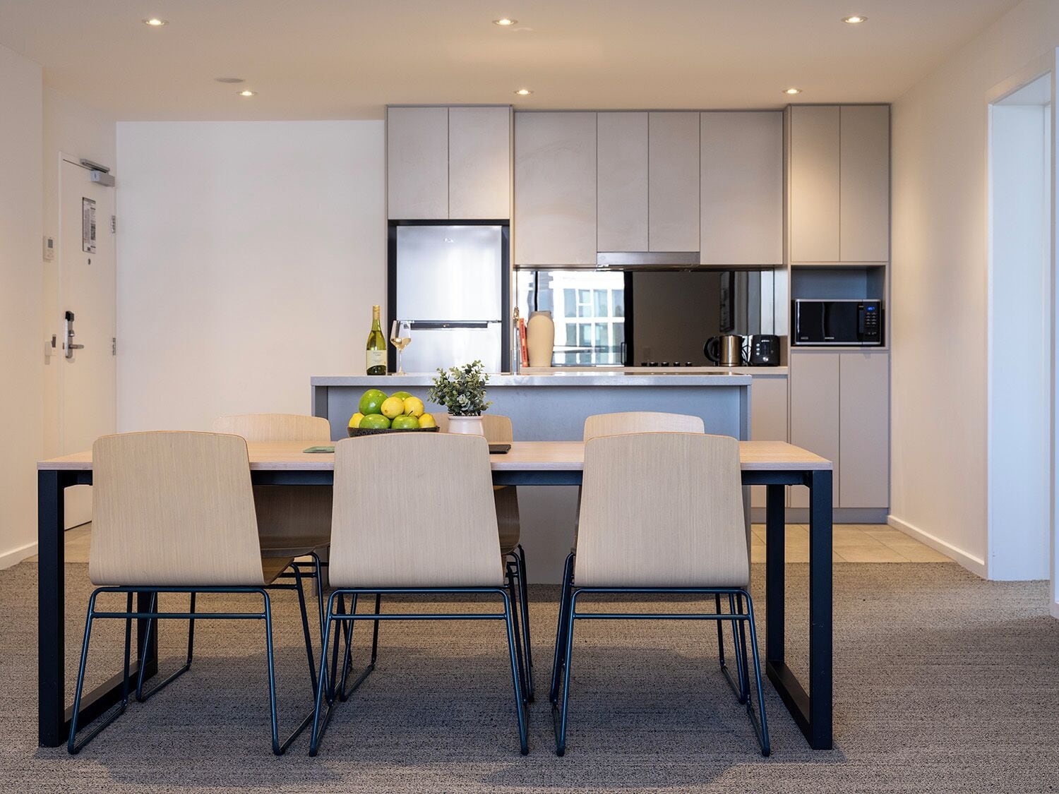 A modern kitchen with a dining area, featuring a table with chairs, a refrigerator, a microwave, and a potted plant.