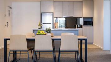 A modern kitchen with a dining area, featuring a table with chairs, a refrigerator, a microwave, and a potted plant.
