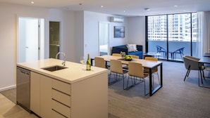 A modern apartment with a kitchen, dining area, and a balcony with a city view. - Quest Robina (Robina)