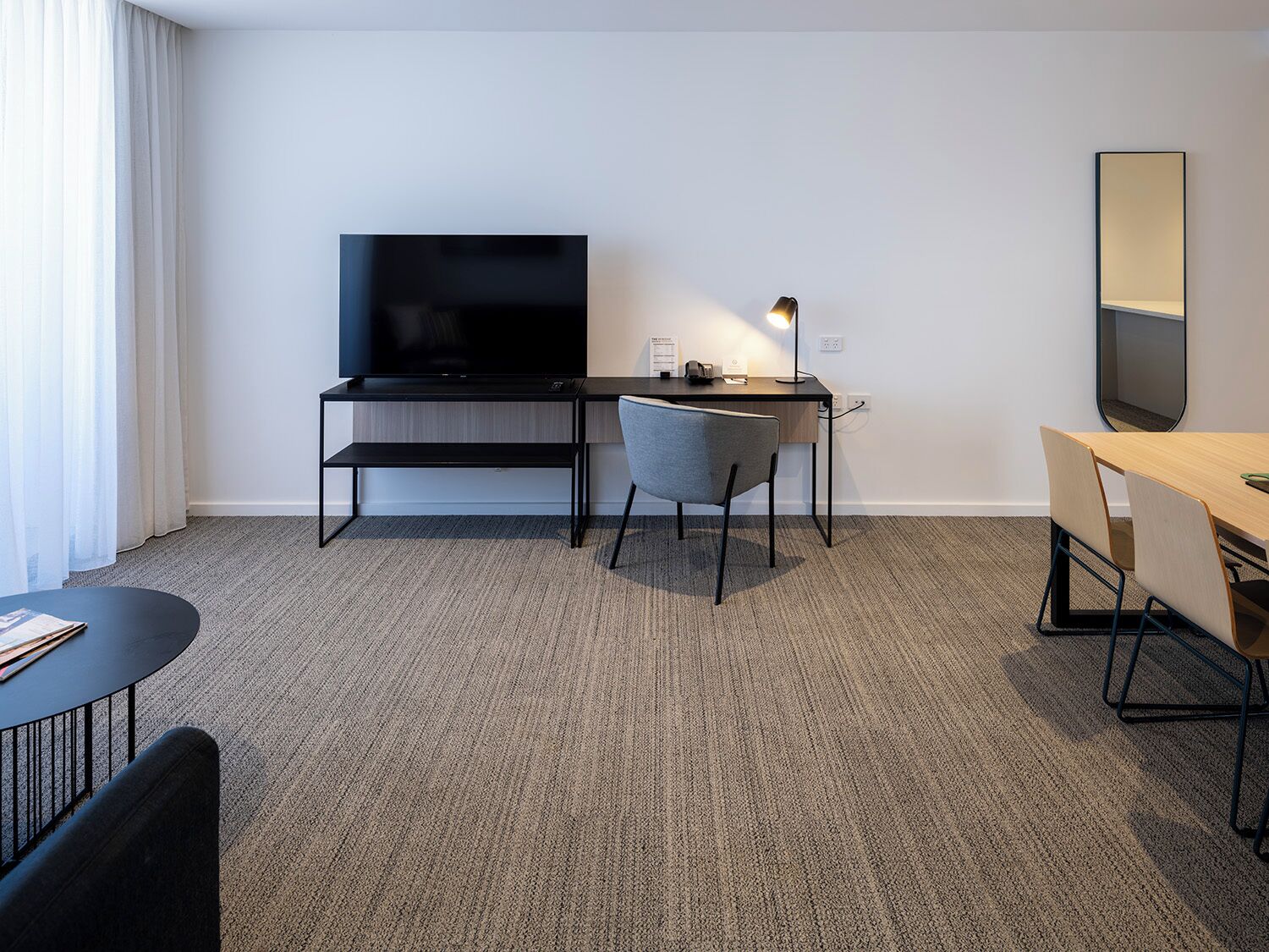 Habitación de hotel con televisión de pantalla plana, un escritorio con silla, una mesita y un espejo en la pared.