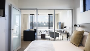 A modern hotel room with a large bed, a desk, a chair, and a balcony with a view. - Quest Robina (Robina)