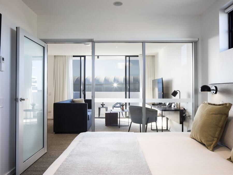 A modern hotel room with a large bed, a desk, a chair, and a balcony with a view.