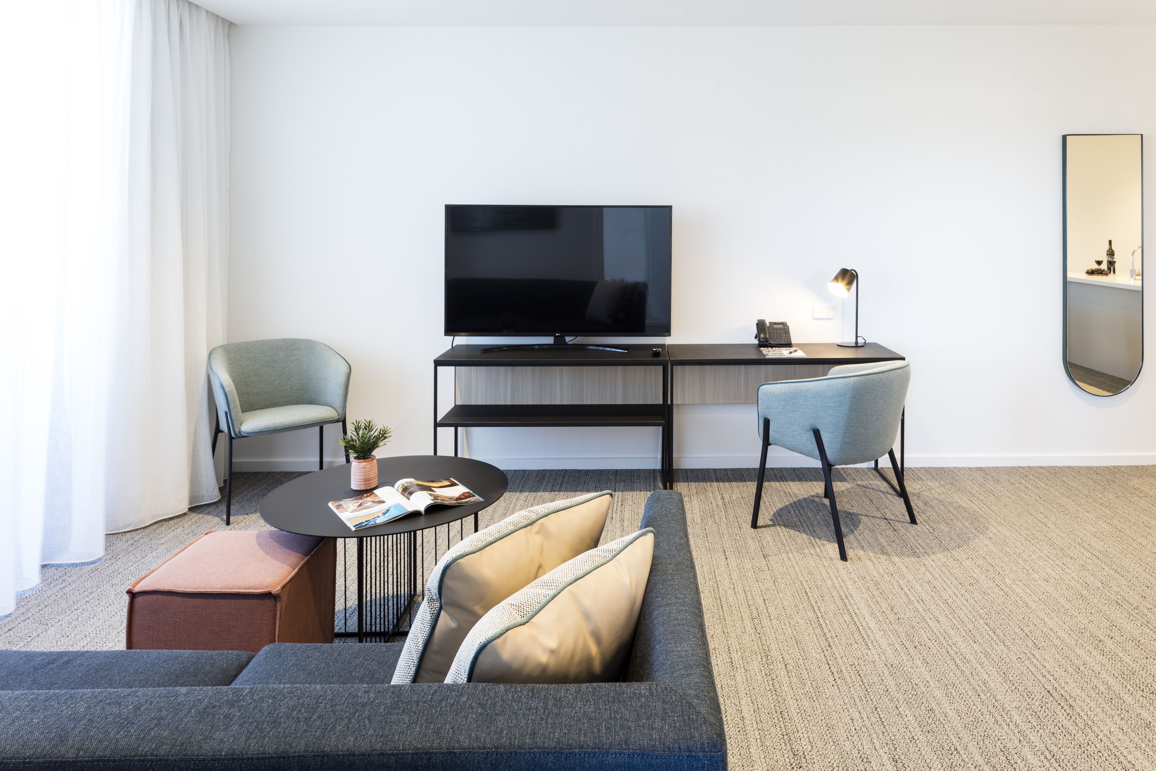 A modern hotel room with a flat-screen TV, a desk, two chairs, a sofa, and a small coffee table.