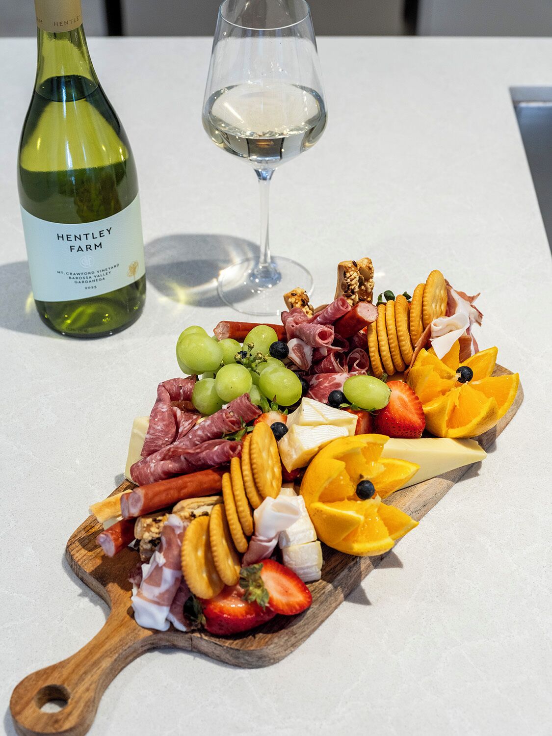 Eine Platte mit verschiedenen Wurstwaren, Käsesorten, Obst und Crackern, dazu eine Flasche Wein und ein Weinglas.