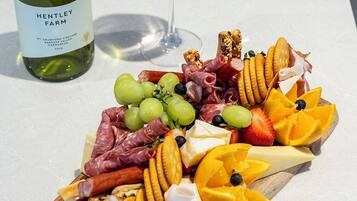 Eine Platte mit verschiedenen Wurstwaren, Käsesorten, Obst und Crackern, dazu eine Flasche Wein und ein Weinglas.