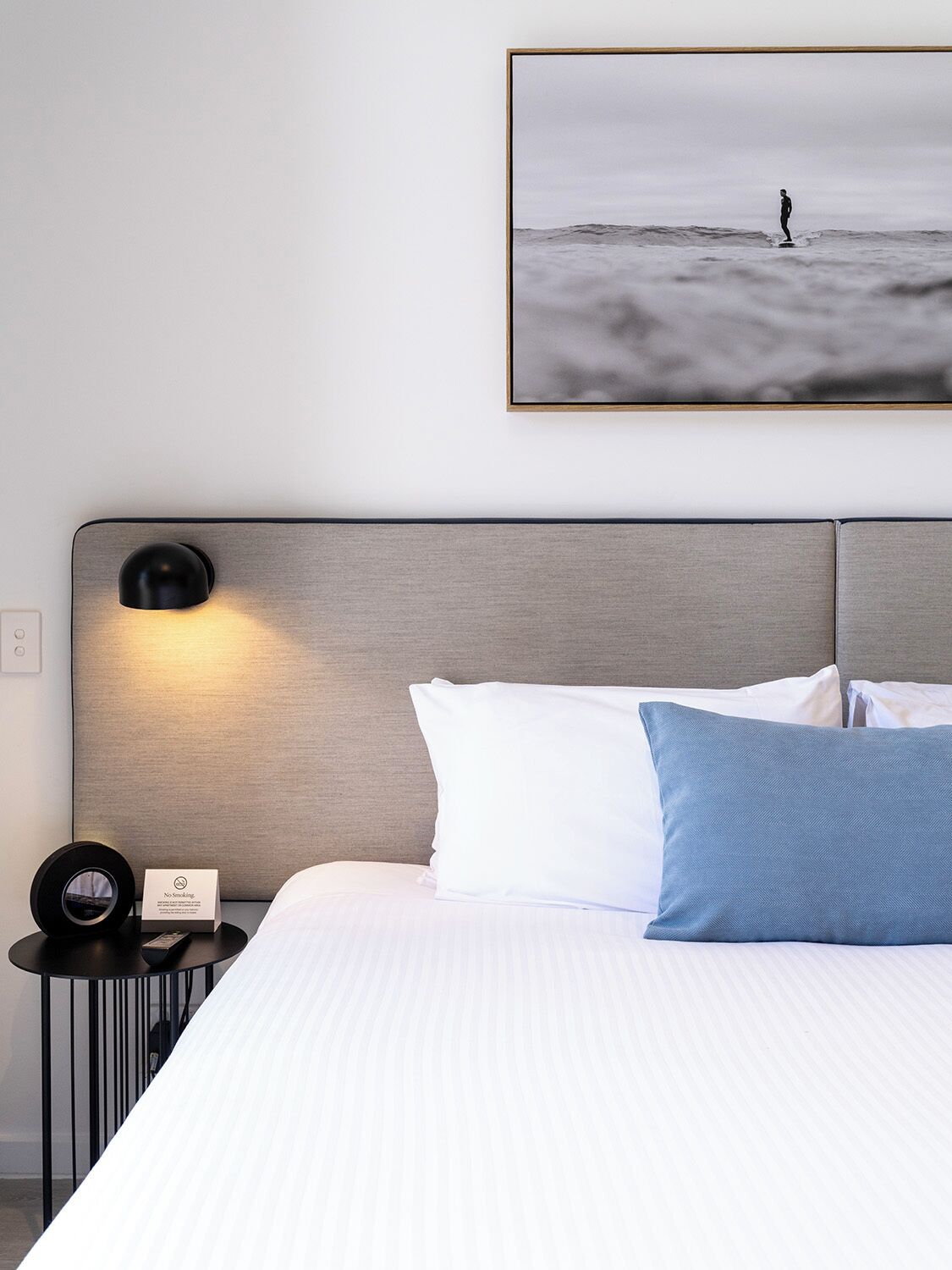 Een hotelkamer met een bed, een nachtkastje met een lamp, een lijst met een foto aan de muur en een bordje met de tekst 'niet roken'.