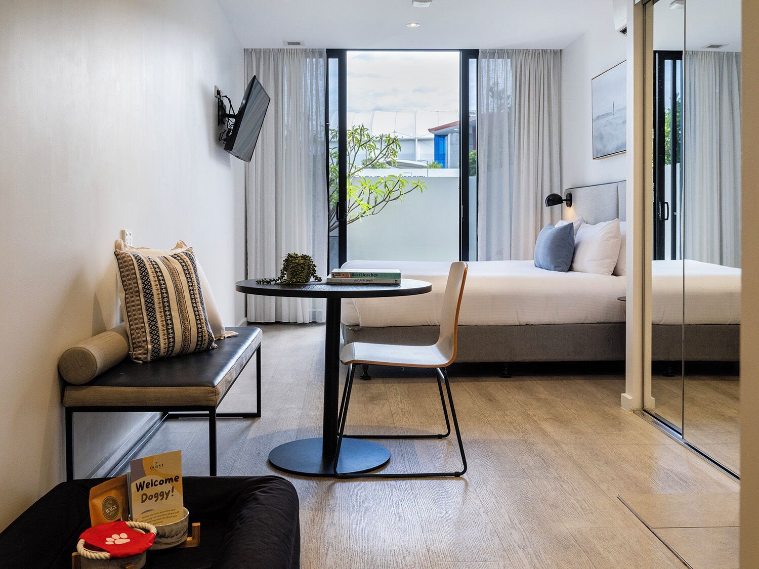 Una habitación de hotel moderna con sofá, una mesita redonda, cama y televisor montado en la pared.